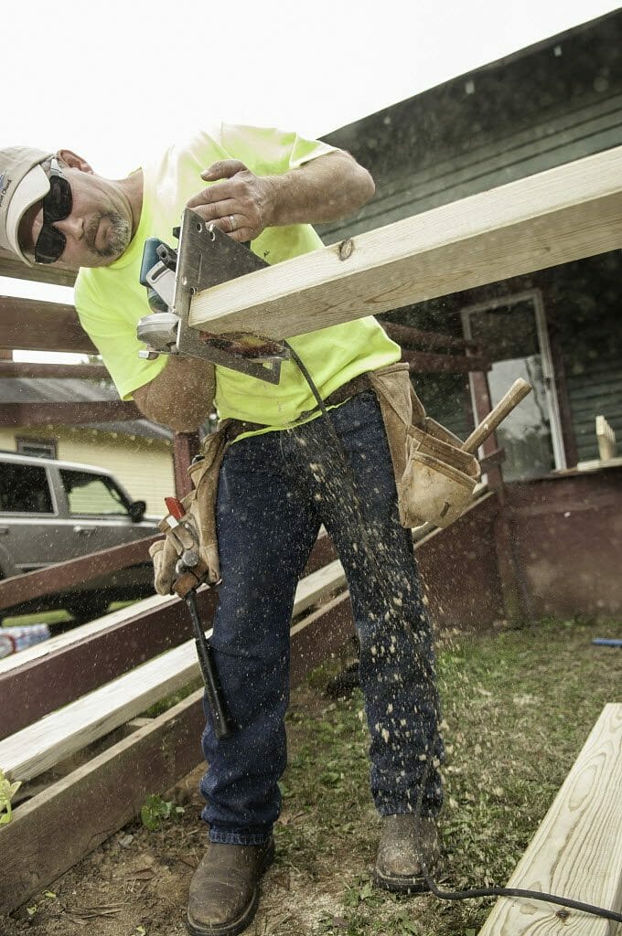 A male volunteer using a saw on a wooden beam